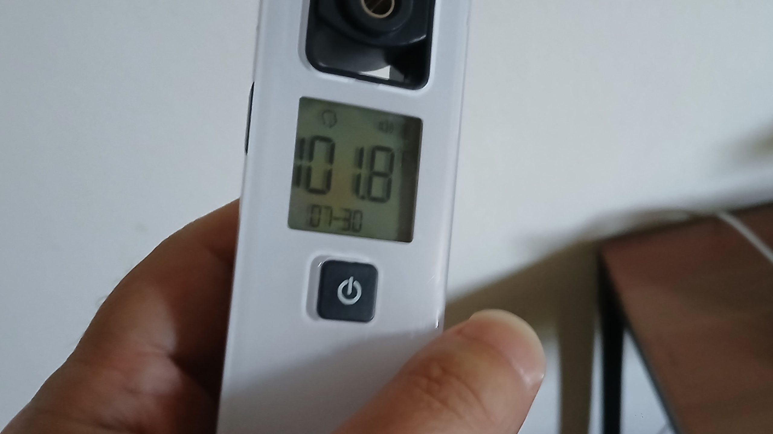 A person's left hand holds an infrared thermometer. The digital readout says: 101.8° F, 7-30