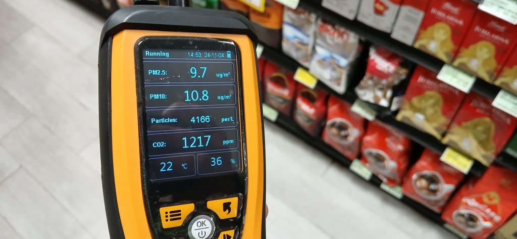 An orange Temtop air quality monitor shows 9.7 parts per million of PM2.5 particulate matter, 10.8ppm of PM10, 4166 particles per liter and 1217ppm CO2, at 22 degrees Celsius and 36% relative humidity, in a supermarket aisle.