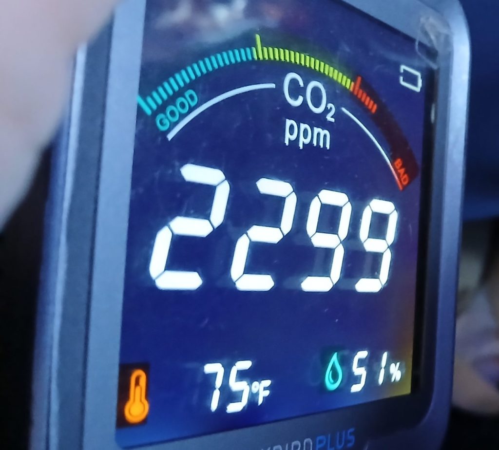 In an airplane seat, an INKBIRD carbon dioxide monitor reads 2299 parts per million, 75 degrees Fahrenheit and 51% relative humidity.